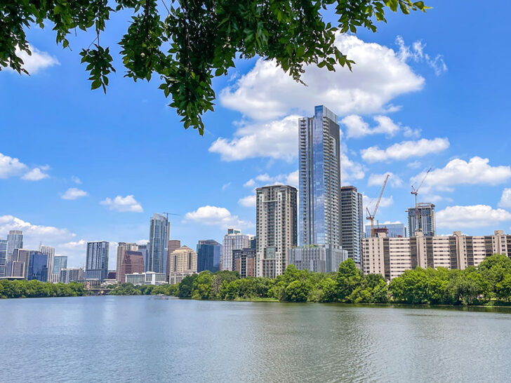 Tall modern buildings in a town from a across a river with some treest beside it, a must view to see in 3 days in Austin Texas