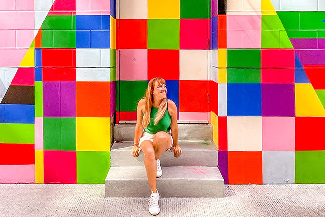 Me sitting in the entrance of a doorway with walls covered by colorful square paintings forming a triangle in the middle.
